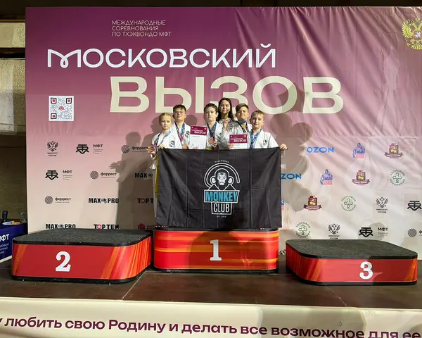 Ученики Monkey Club с медалями и дипломами держат флаг клуба на пьедестале турнира по тхэквондо МФТ "Московский вызов"