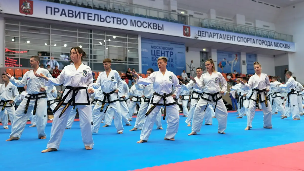 Спортсмены с чёрными поясами строем выполняют технику в большом спортивном зале