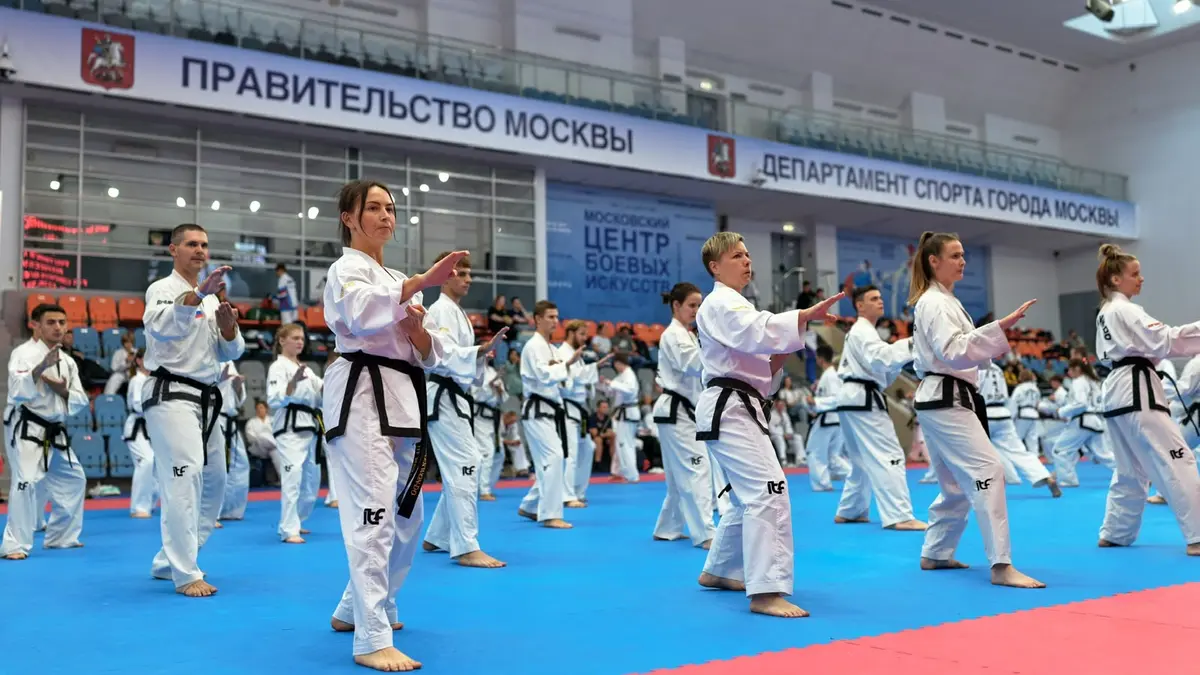 Спортсмены с чёрными поясами стоят рядами и одновременно выполняют движение в большом зале